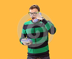Ahgry young man talking on the phone. Man holds purple phone in his hands and calling on a yellow background. Man with open mouth