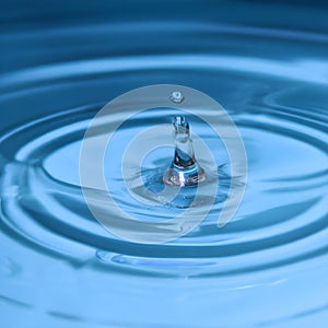 AI generated illustration of a single blue water droplet isolated in a shallow pool of liquid