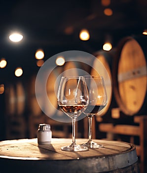 AI generated illustration of two wine glasses on a table near winery barrels
