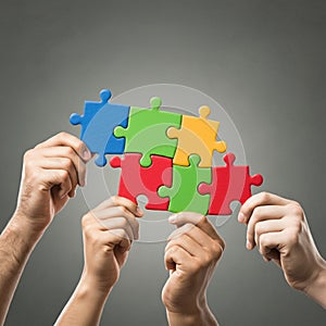 AI-Generated Image of Four Hands Connecting Colorful Puzzle Pieces Against Gray Background photo