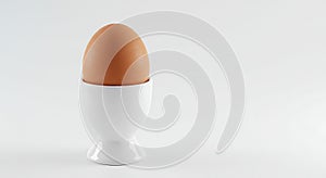 a single brown egg in a white egg cup on a white background - generated using ai