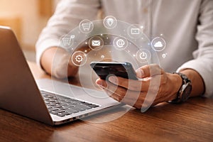 AI generated user holding smartphone while using laptop with floating service icons representing connected digital lifestyle