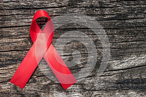 Aids red ribbon for World aids day and national HIV/AIDS and aging awareness month concept. Symbolic satin bow isolated on wood