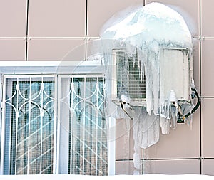 Air conditioner covered with frozen ice and icicles. Near the window