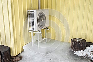 Air conditioner machine outdoors on rack on domestic home house yellow wall.