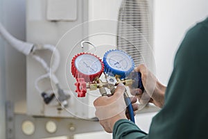 Air conditioning, HVAC service technician using gauges to check refrigerant and add refrigerant.