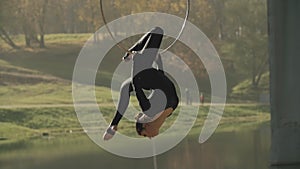 Air gymnastics woman performs acrobatics trick on aerial hoop. Flexible brunette