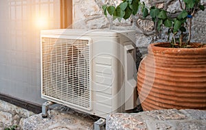 Air heat pump outdoor unit against wall of Greek house.