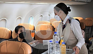 Air hostess  wearing protective face mask service  for passengers on the airplane ,Cabin crew pushing service cart and serve to cu
