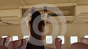 A air hostess woman is reaching into an overhead compartment on an airplane