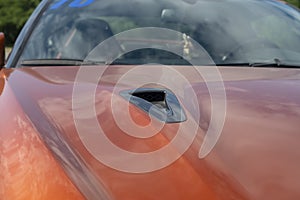 Air intake on the hood of an orange sports car.