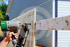 Air nail gun is used by a man to nail planks together to create wooden fence around his yard