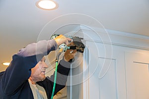 Air nailer tool carpenter using nail gun to crown moldings on kitchen cabinets with white cabinets