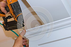 Air nailer tool carpenter using nail gun to crown moldings on kitchen cabinets with white cabinets