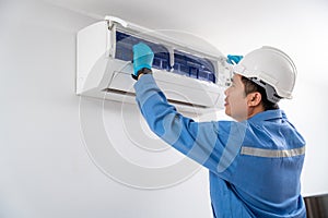 Air technician wearing blue uniform service checking and repairing air conditioner on white wall. Service concept of an air