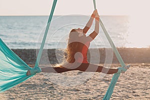 Air yoga on the open air beach. Woman doing split on hammock.