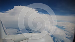 Aircraft flying in clouds airplane Wing and blue sky as seen by passenger through airplane porthole