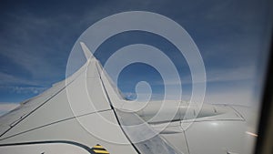 Aircraft flying in clouds airplane Wing and blue sky as seen by passenger through porthole windows. Wide footage