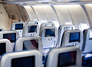 Aircraft interior with seats and blank touch screens displays.