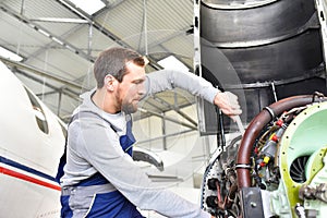 Aircraft mechanic repairs an aircraft engine in an airport hangar