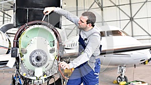 Aircraft mechanic repairs an aircraft engine in an airport hangar