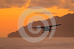 Aircraft on the orange sky with dark clouds. Airplane in the wil nature. Forest hill near the ocean water. Air travelling in Costa