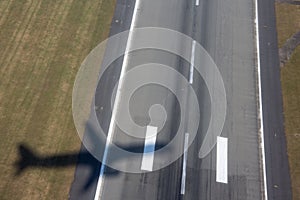 Aircraft shadow after takeoff on ground over airport runway with green grass