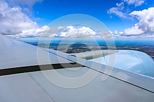 Aircraft wing against blue sky with fluffy cumulus clouds