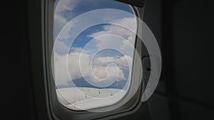 Aircraft Wing of flying in clouds and blue sky airplan. View from passenger porthole windows.