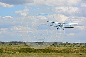 The airplane AN-2 is coming down over green grass for landing