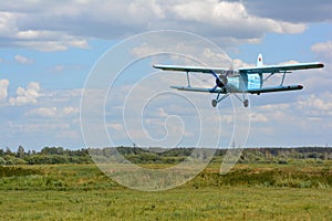 The airplane AN-2 is coming down over green grass for landing