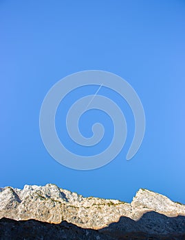 Airplane above Alps mountains. Airplane trail in clear blue sky in Alps. Travel destinations concept.