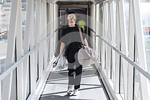 Female passenger carrying the hand luggage bag, walking the airplane boarding corridor.