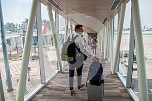 Casual male passenger carrying the hand luggage bag, walking the airplane boarding corridor.