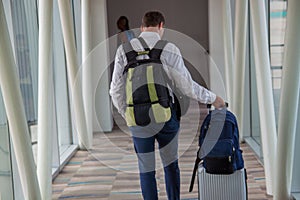 Casual male passenger carrying the hand luggage bag, walking the airplane boarding corridor.