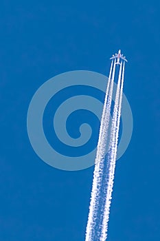 Airplane at cruising altitude seen from below with white contrails and a clear blue and cloudless sky
