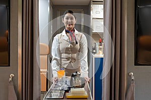 Airplane flight attendant leading trolley cart through plane aisle to serve passengers for food and drinks on board