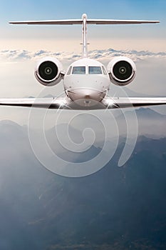 Airplane fly over clouds and Alps mountain on sunset. Front view of a big passenger or cargo aircraft, business jet