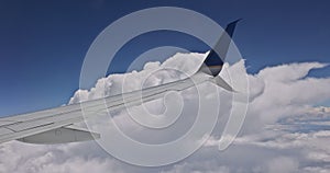 Airplane flying above clouds in aircraft wing on blue sky background.