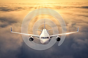 Airplane is flying above the clouds at sunset in summer