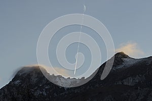 Airplane flying above mountain peak with fog at sunset