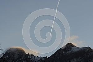 Airplane flying above mountain peak with fog at sunset