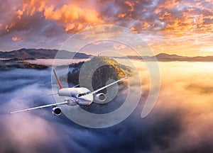 Airplane is flying above mountain peak in low clouds at sunrise