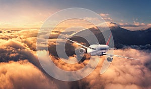 Airplane is flying above mountain peak in orange low clouds