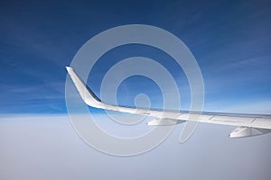 Airplane flying above snowy mountains landscape on a sunny day, view from plane window of clouds and wing turbines