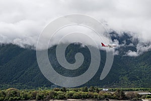 Airplane flying through the clouds over the pine forest covered mountains