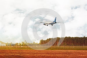 Airplane flying down near field and forest