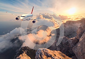 Landscape with white passenger airplane, mountains, sea and orange sky photo