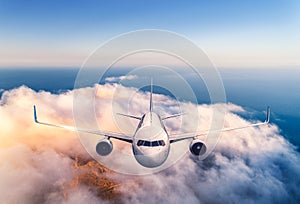 Airplane is flying over the clouds at sunset in summer. Aircraft