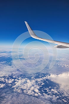 Airplane flying over color sky clouds during scenic sunset or sunrise cloudscape, view from plane window of wing turbines and